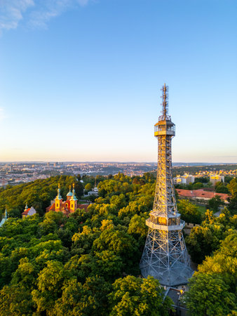 Petrin Lookout Tower rises majestically, surrounded by lush greenery and historic buildings. The sunrise bathes Prague in warm hues, enhancing the scenic beauty of the city.の写真素材