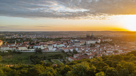 At sunrise, Prague Castle stands majestically against a vibrant sky, casting warm golden hues over the citys rooftops and lush greenery, capturing the essence of this historic site.の写真素材