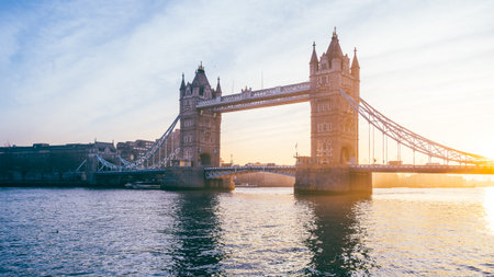 Tower Bridge stands majestically at sunrise, bathed in warm hues, with the River Thames reflecting the soft morning light in the heart of London, UK.の写真素材