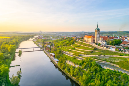 Aerial view captures Melnik City and its historic chateau perched above the serene Labe River. The landscape features lush greenery and tranquil waters during golden hour.の写真素材