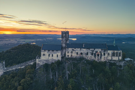 Bezdez Castle stands majestically on a hilltop, bathed in the warm glow of sunset. This medieval ruin offers stunning views of the surrounding countryside, vibrant with summer hues.の写真素材