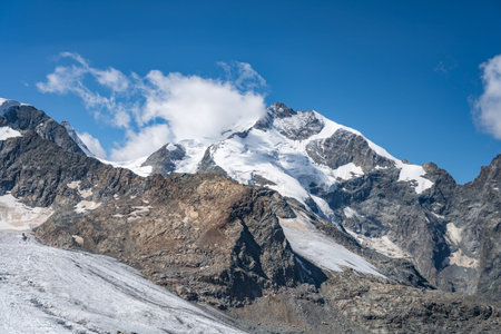 Piz Bernina rises prominently in the Swiss Alps, showcasing its snow-capped peak and glacier. The surrounding rocky landscape highlights the beauty of this alpine region on a clear day.の写真素材