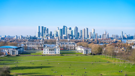 Greenwich Park showcases its vast green space, while the modern buildings of London rise prominently in the background. People enjoy leisure activities throughout the park.の写真素材