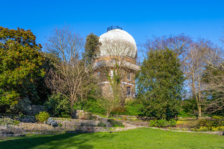 Visitors enjoy the scenic beauty of the Old Royal Observatory in Greenwich, surrounded by lush green gardens and trees, under a clear blue sky on a sunny day.の写真素材