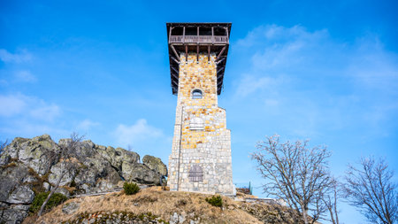 The lookout tower stands tall on Wysoki Kamien surrounded by rocky terrain and trees in the Jizera Mountains of Poland. Clear blue skies enhance the scenery, inviting exploration.の写真素材