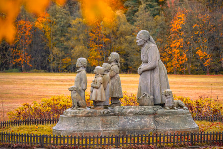 A touching statue of a grandmother and her grandchildren stands in Granny Valley, Ratiborice, Czechia. The scene is framed by colorful autumn leaves, capturing a moment of love and nostalgia.の写真素材