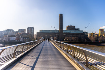 People stroll over a modern bridge leading to the Tate Modern gallery in London, surrounded by cityscape. Its a clear day, perfect for enjoying the vibrant atmosphere along the river Thames.の写真素材