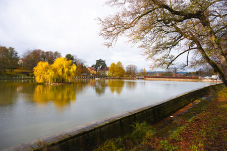 Autumn scenery at the spa pond in Kudowa Zdroj showcases vibrant colors and tranquil waters. Trees display golden leaves, reflecting on the calm surface, creating a peaceful atmosphere.の写真素材