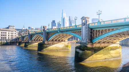 Bright sunlight reflects off the Thames River as Southwalk Bridge stands proudly in London. The bridge connects the bustling cityscape with scenic views along the riverbank.の写真素材