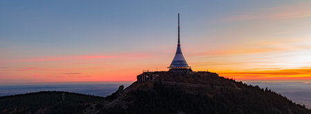 Aerial view shows Jested mountain with a hotel at sunset. The sky is filled with colors as the sun...