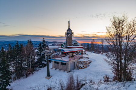Tanvaldsky Spicak Ski Resort shows the lookout tower surrounded by winter snow. The scene captures the mountains with trees in the background. Sunset colors fill the sky above.の写真素材