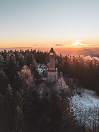 Stepanka lookout tower nestled among the trees of the Jizera Mountains during winter. The sunset casts warm colors over the snow-covered landscape.の写真素材