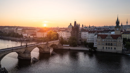 Golden light bathes Charles Bridge in Prague during a peaceful sunrise. The Vltava River reflects the vibrant colors, while historic buildings frame the picturesque view, creating a serene atmosphere.の写真素材