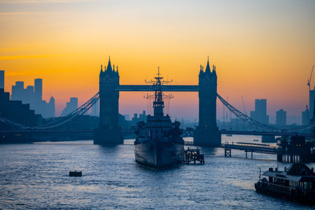 At dawn, the river Thames shows the silhouette of Tower Bridge and HMS Belfast. The scene captures...