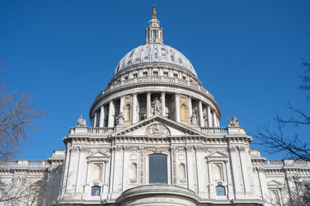 St Pauls Cathedral stands tall against a blue sky in London, UK. The dome is visible along with the detailed architecture and sculptures. Visitors appreciate the historical significance.の写真素材