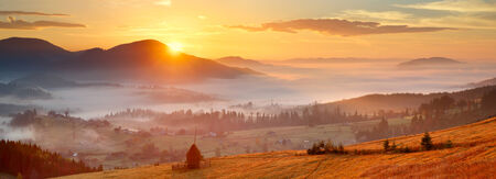 sunrise, mountain village in the fog and everything nice in yellow lightの写真素材