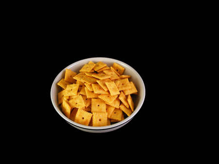 A bowl of cheese crackers against a black background.の写真素材