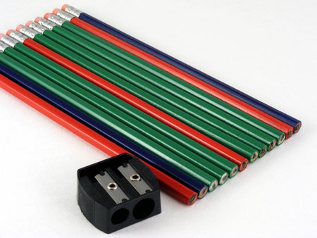 Red, green and blue pencils and a hand sharpener against an off-white background.の写真素材