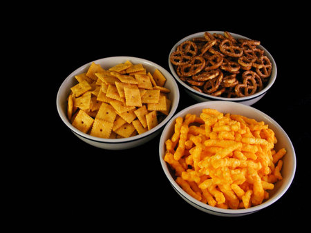 Bowls of cheese snacks, pretzels and cheese crackers against a black background.の写真素材