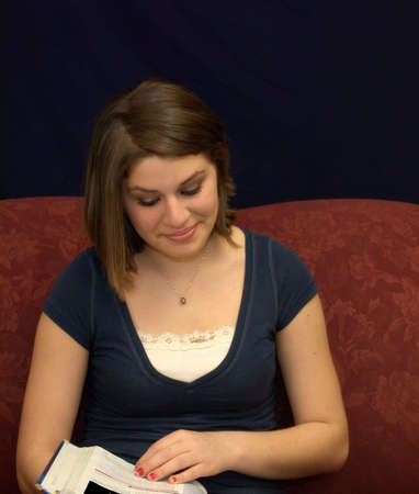 A pretty teenage girl sitting on a sofa studying a textbook.の写真素材