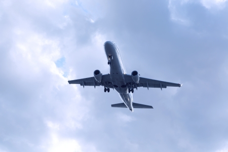 blue passenger airplane flying midair with cloudy skyの写真素材