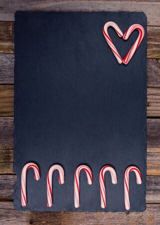Five holiday striped candy canes in a row and a heart shape on dark board and wooden background. Top view, flat lay.の写真素材