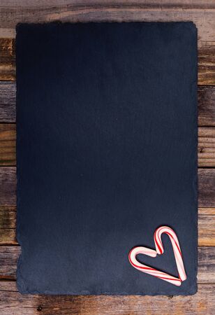 Holiday striped candy canes in heart shape on dark stone board and wooden background. Top view, flat lay.の写真素材