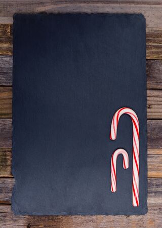 Holiday striped candy canes on dark stone board and wooden background. Top view, flat lay.の写真素材