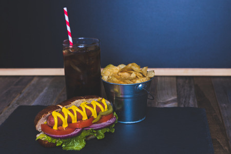 Gourmet hot dog with chips and drink on dark background. Tabletop, front view.の写真素材