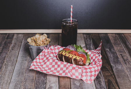 Gourmet hot dog with chips and drink in a basket with gingham napkin. Tabletop, front view.の写真素材