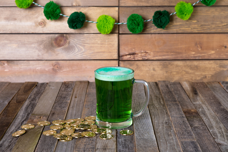 St. Patrickâs mug of green beer with golden coins on wooden background. Tabletop, front view.の写真素材