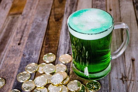 St. Patrickâs mug of green beer with golden coins on wooden background. Tabletop, front view.の写真素材