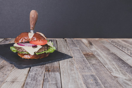 Delicious gourmet cheeseburger with knife on dark wooden backgroundの写真素材