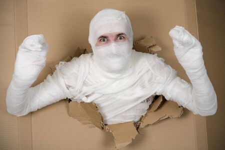 Man in costume mummy looking through hole in cardboardの写真素材