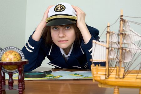 Scared girl in sea uniform at a table with mapの写真素材
