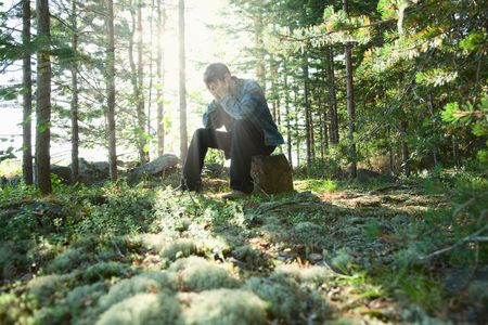The sad young man sits in wood on a stoneの写真素材