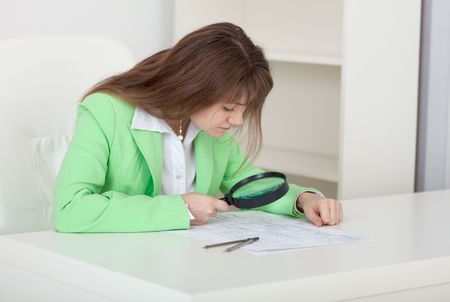 The girl studies drawings by means of a magnifier sitting at a tableの写真素材