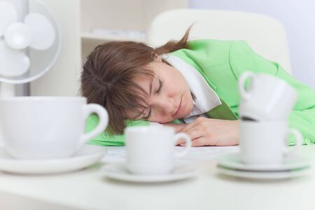 The beautiful woman sleeps on a workplace with coffee cupsの写真素材