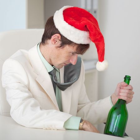 The drunk man in a Christmas cap with a bottle sits at a tableの写真素材
