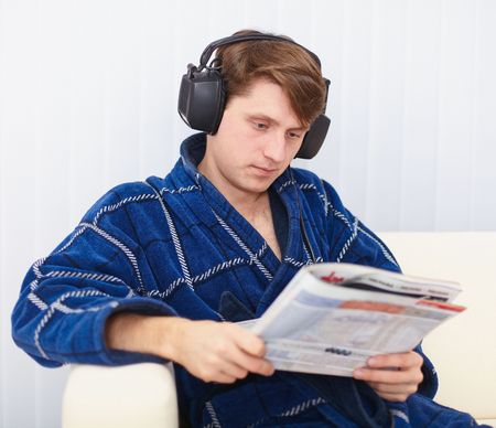 The man in the big ear-phones sits on a sofa reads the newspaperの写真素材