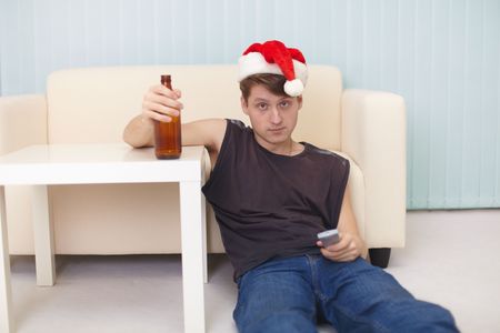 The young man in christmas hat sits on a floor with beer at the TVの写真素材