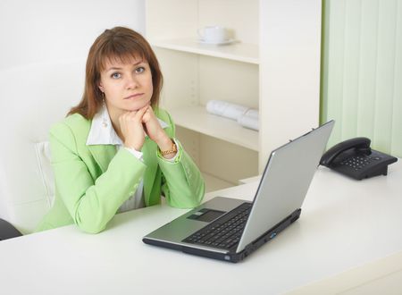 The young woman with the laptop sits at a table at light officeの写真素材