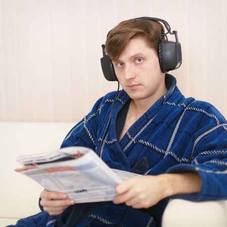 Person in the big ear-phones sits on a sofa reads the newspaperの写真素材