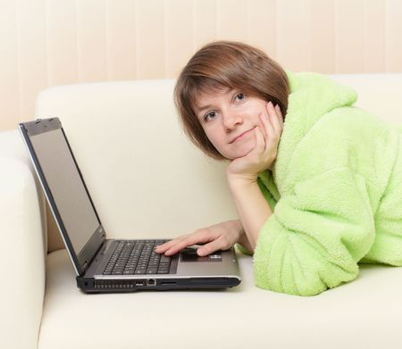 The young woman in a green dressing gown on a sofa with laptopの写真素材