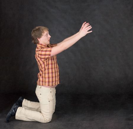 The amusing young man is kneeling and stretch hands to somethingの写真素材