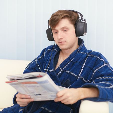 The man in the big ear-phones sits on a sofa reads the newspaperの写真素材