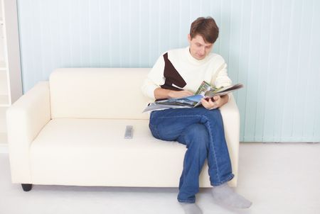 The young man sits on a sofa with the newspaper and remote controlの写真素材