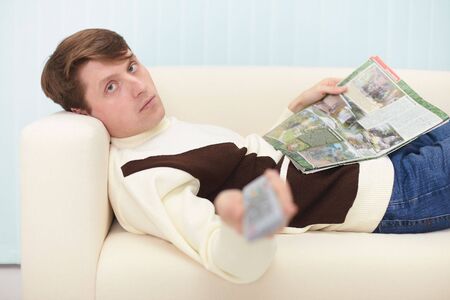 The man with the newspaper has a rest at home on a sofa near the TVの写真素材
