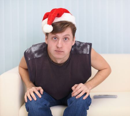 Young man sits on a sofa in a red Christmas capの写真素材