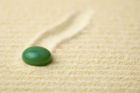 Round green stone on a surface of yellow sandの写真素材